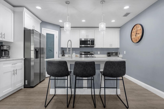 kitchen with pendant lighting, an island with sink, light hardwood / wood-style flooring, white cabinetry, and stainless steel appliances