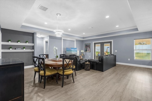 dining space with light wood-type flooring, plenty of natural light, french doors, and a raised ceiling