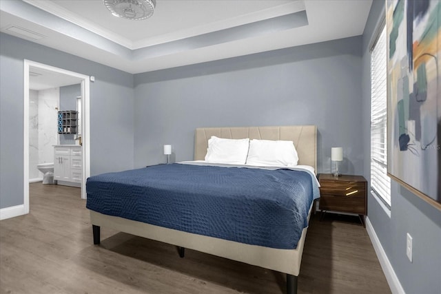 bedroom with a tray ceiling, ensuite bathroom, and dark hardwood / wood-style flooring