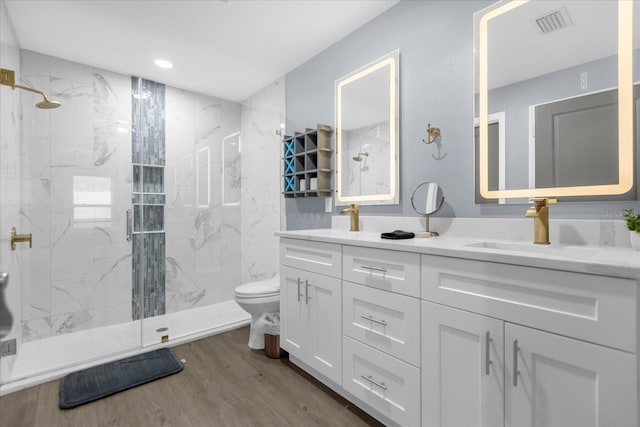 bathroom featuring wood-type flooring, tiled shower, vanity, and toilet