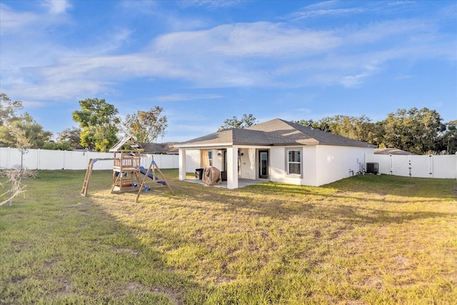 rear view of property featuring a playground, cooling unit, a lawn, and a patio area