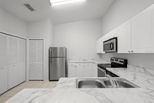 kitchen with white cabinets, light tile patterned flooring, sink, stainless steel appliances, and vaulted ceiling