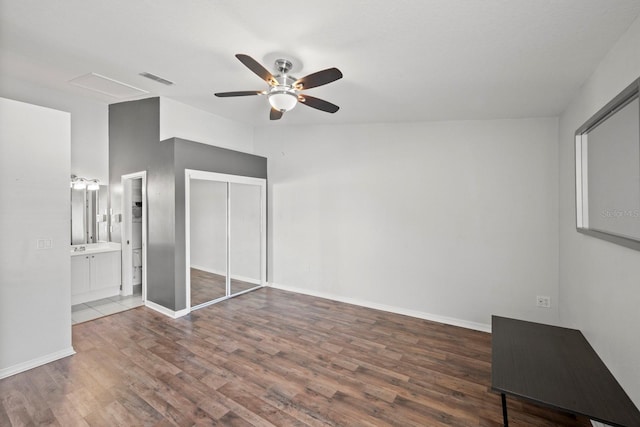 unfurnished bedroom featuring ceiling fan, a closet, ensuite bath, and dark wood-type flooring