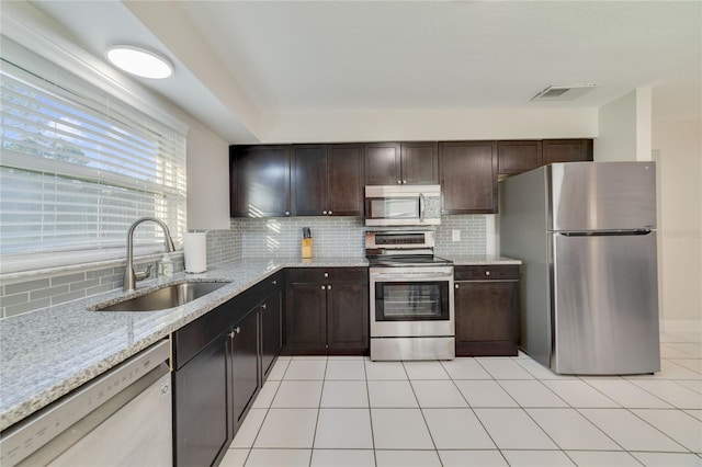 kitchen featuring sink, light tile patterned floors, appliances with stainless steel finishes, tasteful backsplash, and light stone counters