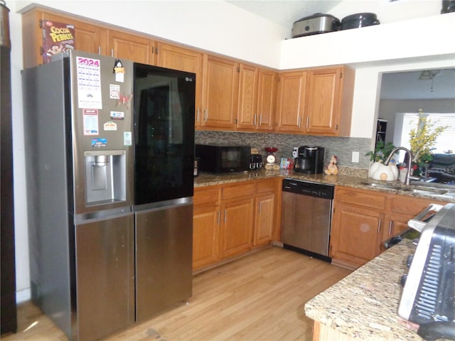 kitchen with light stone countertops, sink, backsplash, appliances with stainless steel finishes, and light wood-type flooring