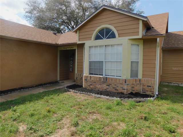 2618 Coventry Ln, Ocoee, FL 34761 - view of exterior entry featuring a shingled roof, a lawn, and brick siding