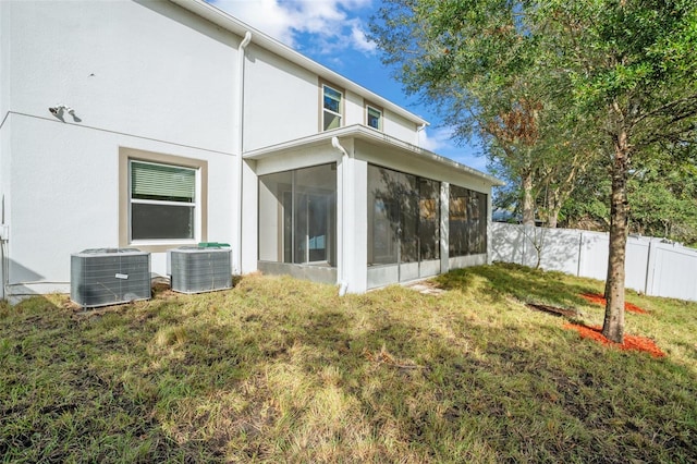 back of house with central air condition unit, a sunroom, and a lawn