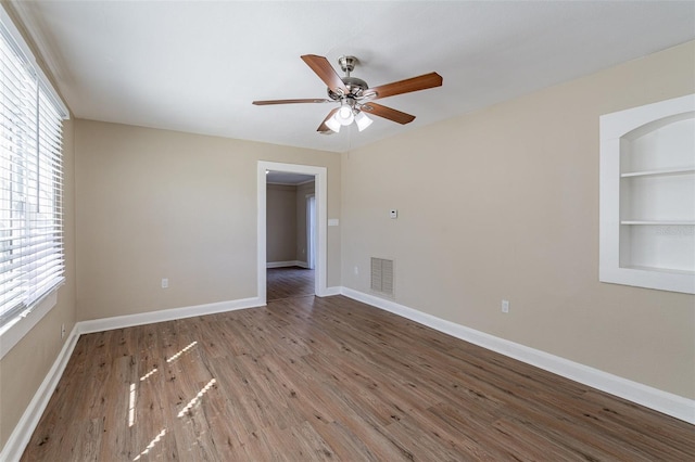 unfurnished room with ceiling fan, built in features, and hardwood / wood-style floors