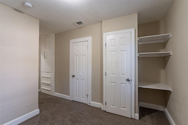 unfurnished bedroom with a textured ceiling and dark colored carpet