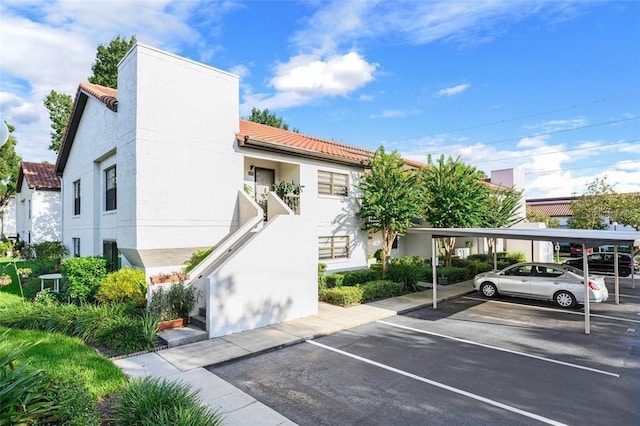 exterior space with stairway, a tile roof, covered and uncovered parking, and stucco siding