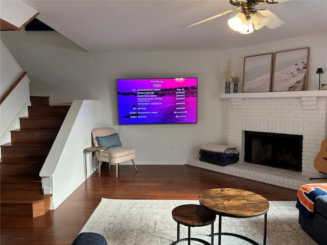 living room featuring baseboards, ceiling fan, stairway, a fireplace, and wood finished floors