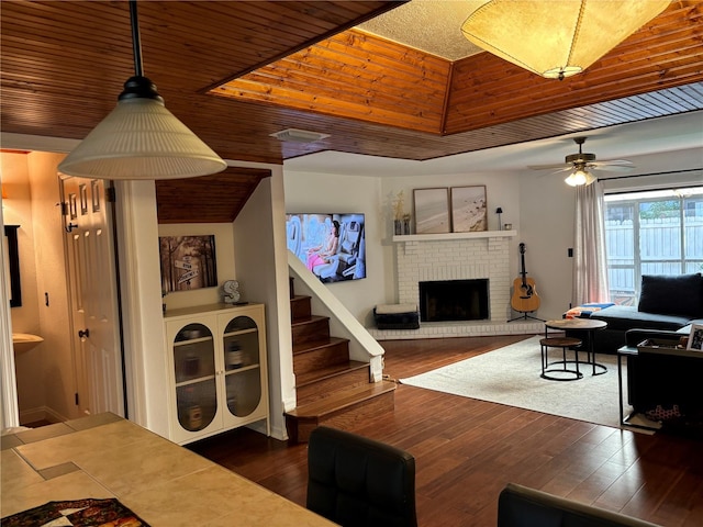 living room with dark wood-type flooring, stairway, wooden ceiling, a fireplace, and a ceiling fan