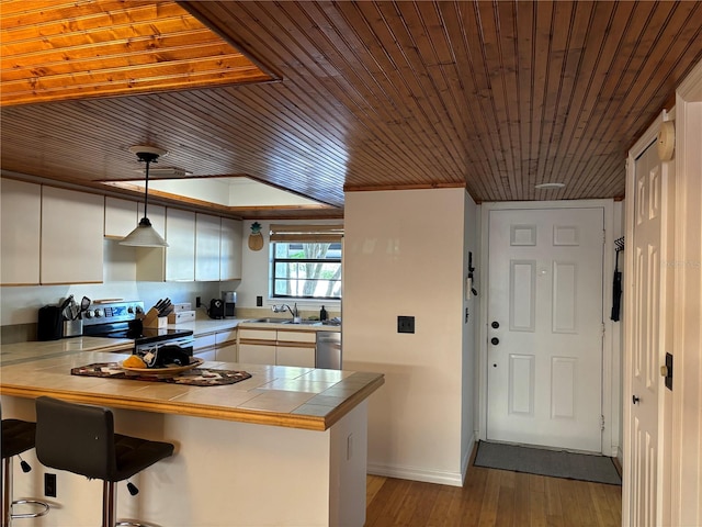 kitchen featuring tile countertops, a peninsula, a sink, white cabinets, and appliances with stainless steel finishes