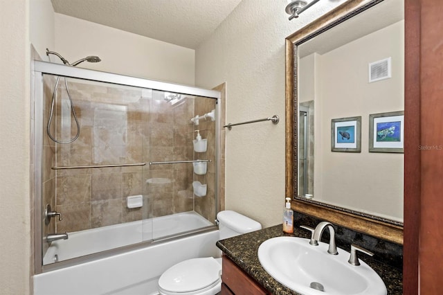 bathroom with visible vents, vanity, a textured wall, toilet, and bath / shower combo with glass door
