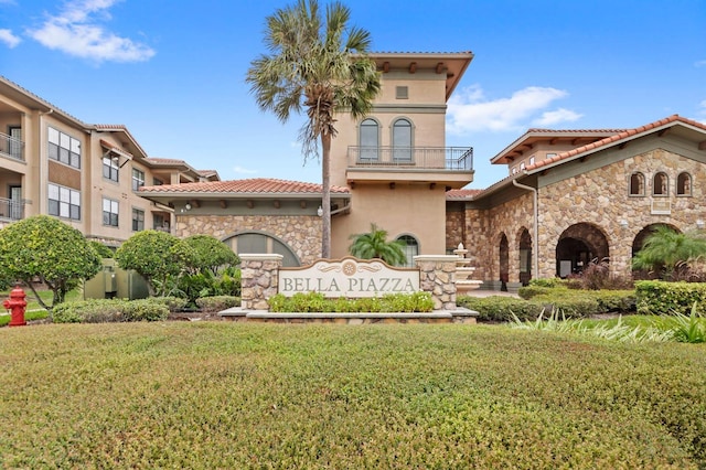 mediterranean / spanish-style house with a front lawn, a tile roof, stone siding, stucco siding, and a balcony