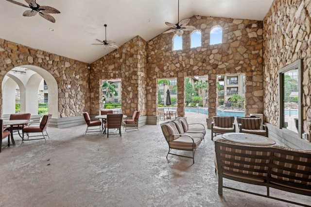 interior space with a ceiling fan, high vaulted ceiling, arched walkways, and unfinished concrete floors