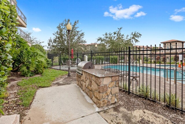 community pool featuring an outdoor kitchen, fence, and area for grilling