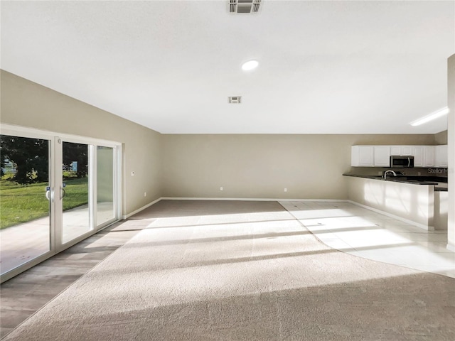 unfurnished living room featuring light carpet and sink