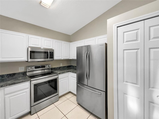 kitchen with white cabinets, stainless steel appliances, light tile patterned floors, and vaulted ceiling