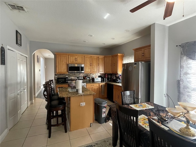 kitchen featuring decorative backsplash, black appliances, a center island, a kitchen bar, and light tile patterned floors