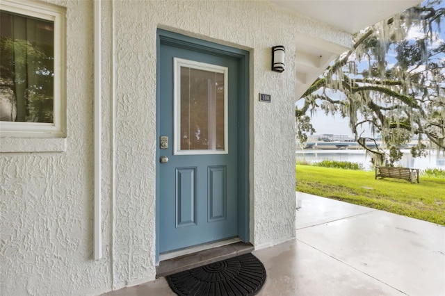 view of exterior entry with a water view and a lawn