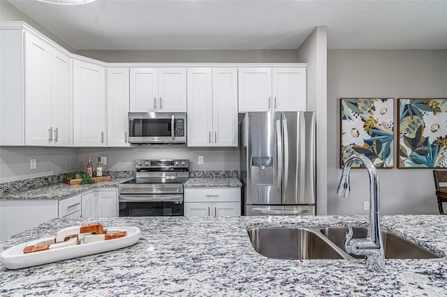 kitchen with white cabinets, stainless steel appliances, sink, and light stone counters