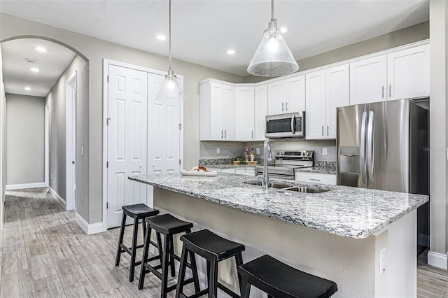 kitchen with white cabinets, hanging light fixtures, a center island with sink, light wood-type flooring, and stainless steel appliances