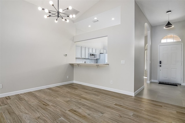 entryway with an inviting chandelier, high vaulted ceiling, and light wood-type flooring