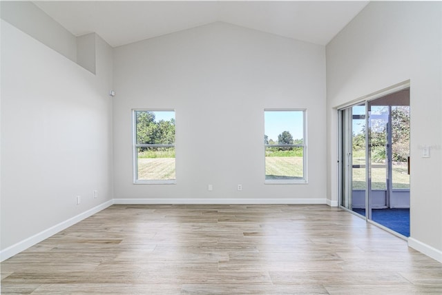 spare room with high vaulted ceiling and light wood-type flooring