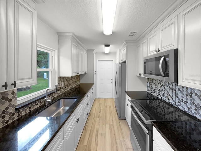 kitchen with stainless steel appliances, dark stone counters, sink, white cabinets, and tasteful backsplash