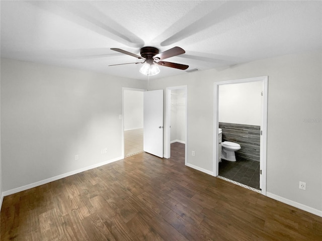 unfurnished bedroom with dark hardwood / wood-style floors, a closet, a spacious closet, ensuite bathroom, and ceiling fan