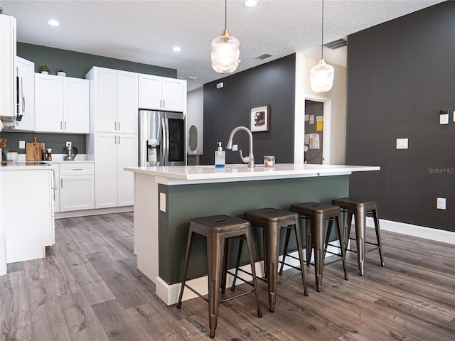 kitchen featuring stainless steel refrigerator with ice dispenser, a center island with sink, and pendant lighting