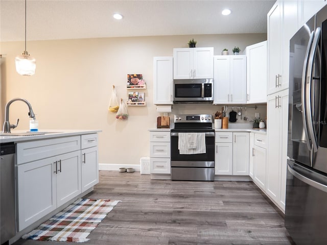 kitchen featuring light hardwood / wood-style floors, white cabinets, stainless steel appliances, and hanging light fixtures