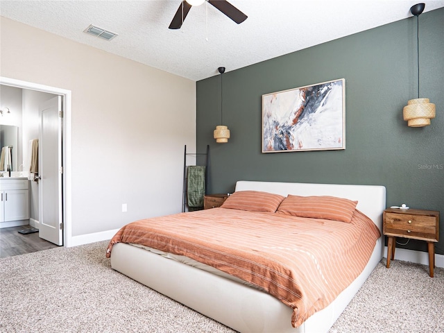 bedroom with a textured ceiling, ensuite bathroom, carpet flooring, and ceiling fan