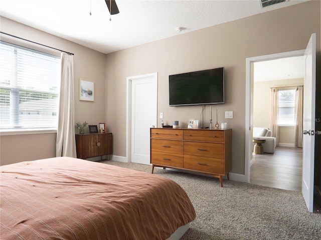 carpeted bedroom featuring a textured ceiling, multiple windows, and ceiling fan