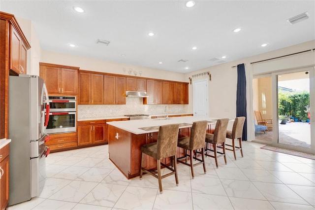 kitchen featuring stainless steel appliances, sink, a center island with sink, a kitchen bar, and backsplash