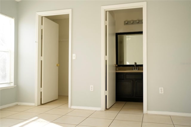 unfurnished bedroom featuring a spacious closet, ensuite bathroom, light tile patterned floors, and sink