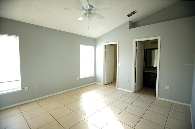 unfurnished bedroom featuring a textured ceiling, ensuite bath, vaulted ceiling, and multiple windows