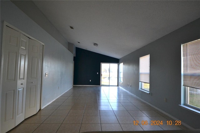 tiled empty room featuring a healthy amount of sunlight, a textured ceiling, and vaulted ceiling