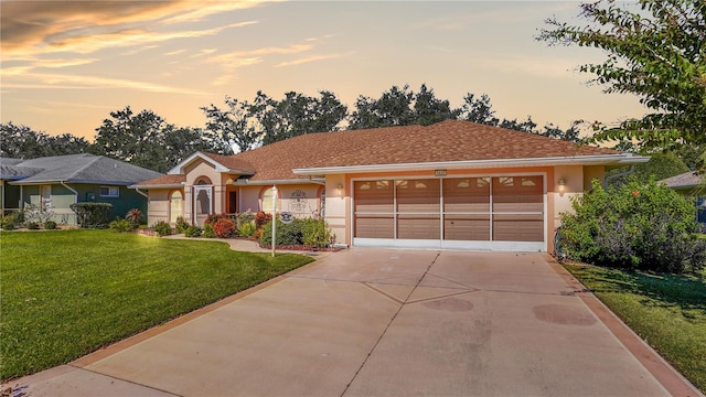 ranch-style house with driveway, a yard, a garage, and stucco siding