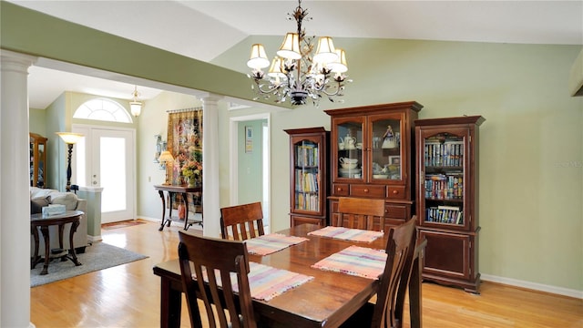 dining area featuring light wood-style floors, a chandelier, vaulted ceiling, and ornate columns