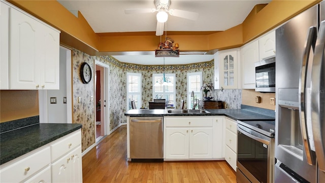 kitchen featuring a peninsula, a sink, appliances with stainless steel finishes, dark countertops, and wallpapered walls