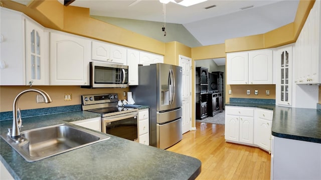 kitchen with stainless steel appliances, dark countertops, a sink, and glass insert cabinets