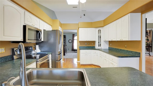 kitchen with appliances with stainless steel finishes, dark countertops, white cabinetry, and light wood-style flooring