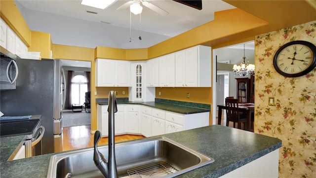 kitchen featuring stainless steel appliances, a sink, white cabinetry, dark countertops, and wallpapered walls