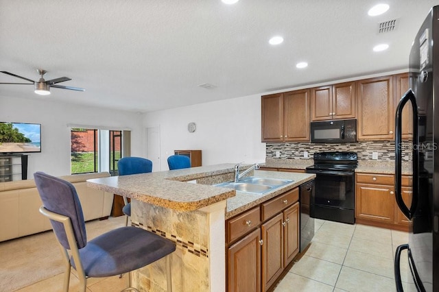 kitchen with a kitchen island with sink, sink, black appliances, light tile patterned floors, and ceiling fan