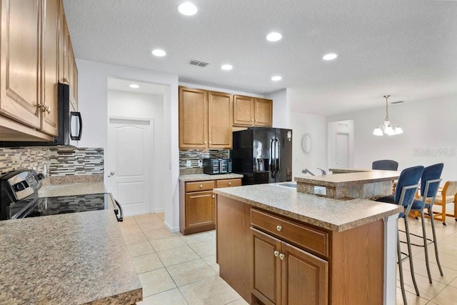 kitchen featuring black appliances, a center island, decorative light fixtures, and a breakfast bar