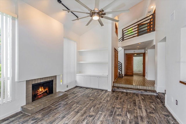 unfurnished living room with a brick fireplace, ceiling fan, high vaulted ceiling, dark hardwood / wood-style floors, and built in shelves