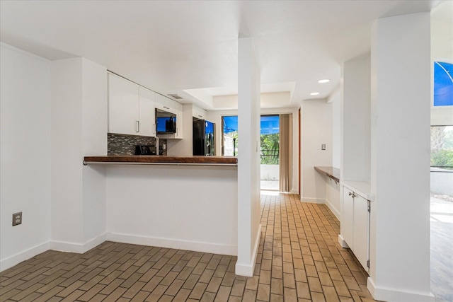 kitchen featuring decorative backsplash, white cabinetry, a healthy amount of sunlight, and black fridge