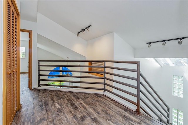 corridor featuring rail lighting, vaulted ceiling, plenty of natural light, and dark hardwood / wood-style floors